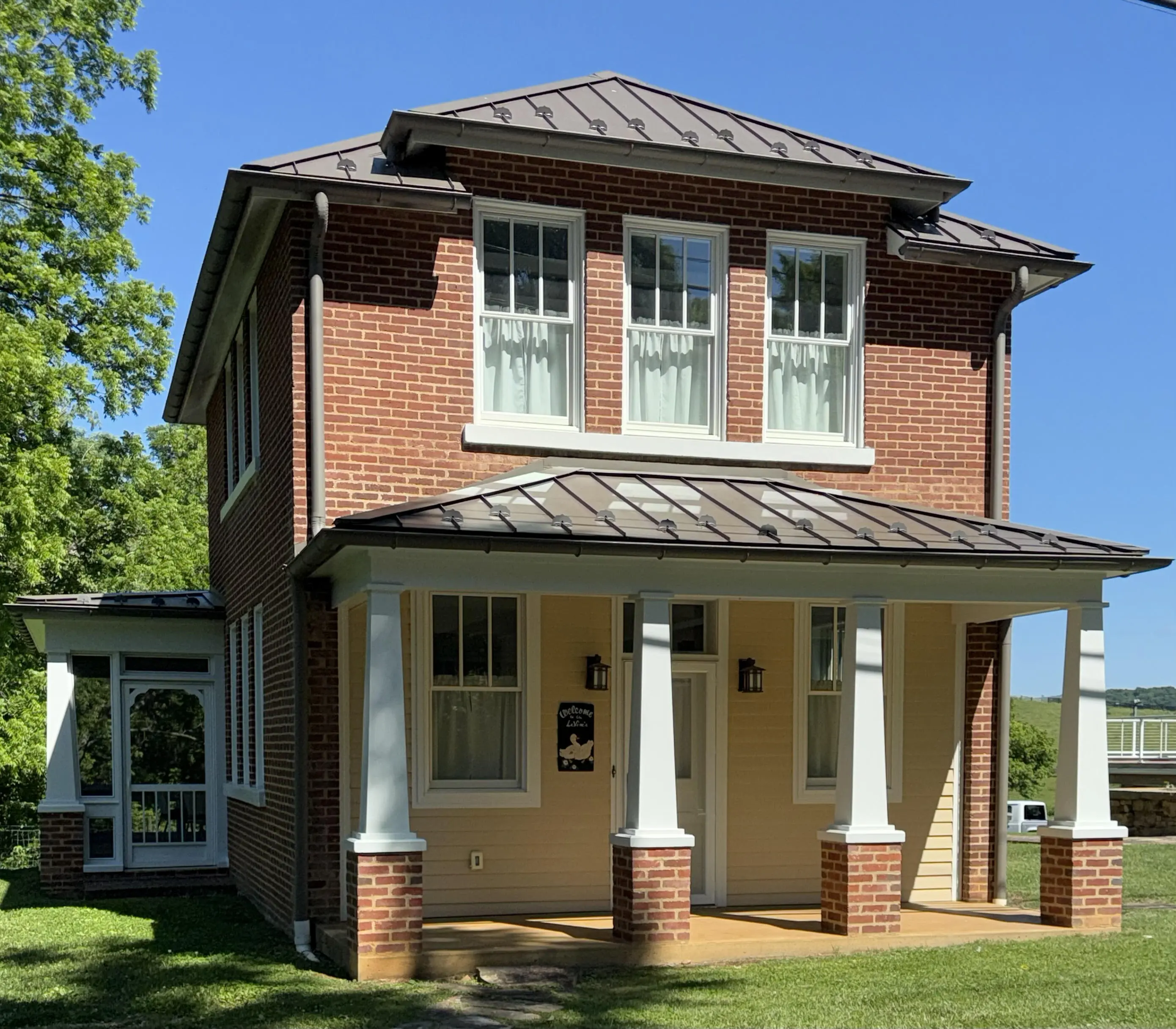 340 Green Spring Rd. Two-story brick house with white pillars and metal roof under clear blue